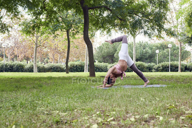 Mitte erwachsene Frau praktiziert Yoga auf Matte im Park — Stockfoto