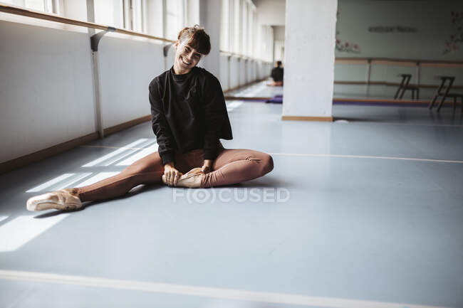 Glückliche Balletttänzerin streckt Beine auf dem Boden im Studio — Stockfoto