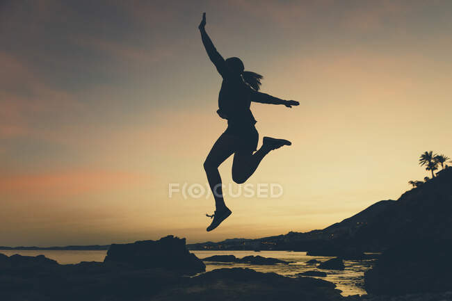Silhueta de mulher pulando na praia durante o pôr do sol — Fotografia de Stock