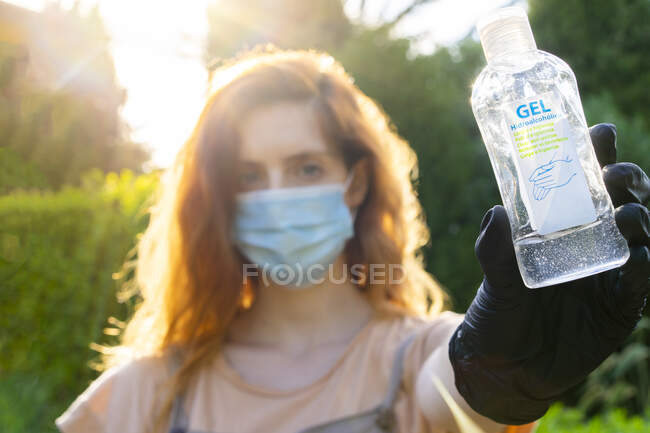 Primo piano della donna che indossa maschera che tiene bottiglia in cortile — Foto stock