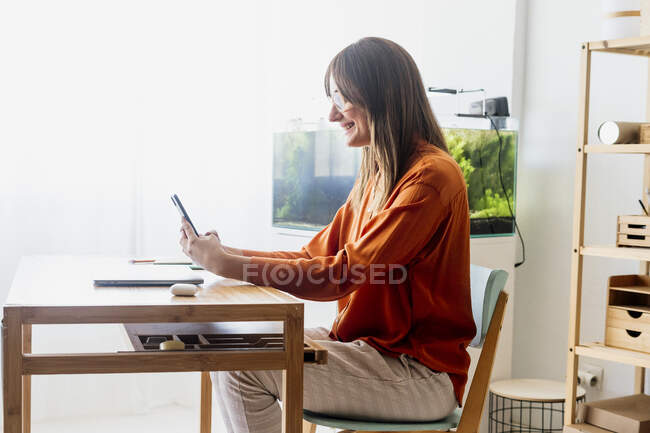 Женщина-фрилансер, работающая дома, сидит за столом со смартфоном — стоковое фото