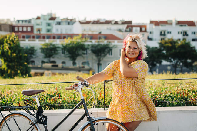 Щаслива жінка плюс розмір з велосипедом, що спирається на паркан — стокове фото