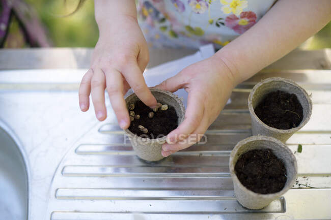 Mains de fille plantant des graines dans de petits pots sur la table au jardin — Photo de stock