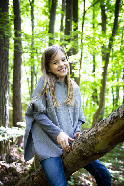 Porträt eines lächelnden süßen Mädchens, das auf einem Baumstamm im Wald sitzt — Stockfoto
