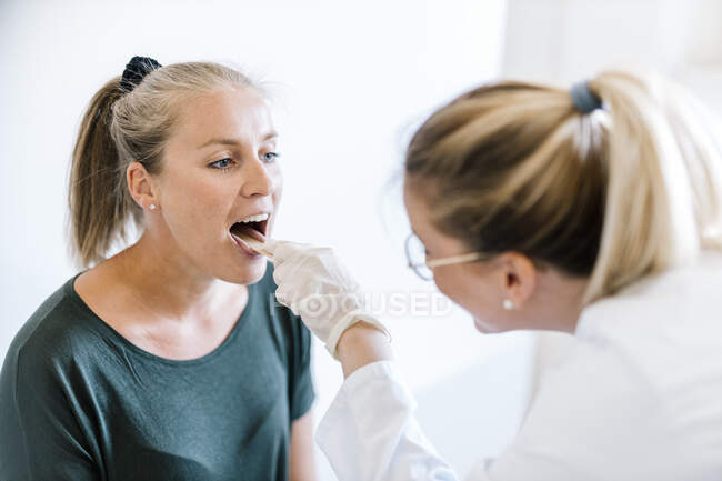 Female doctor examining female patient with tongue depressor — Stock Photo