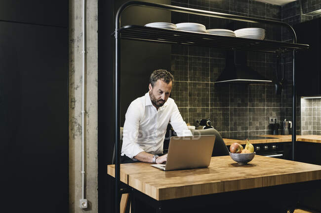 Uomo d'affari maturo che lavora in cucina, utilizzando laptop — Foto stock