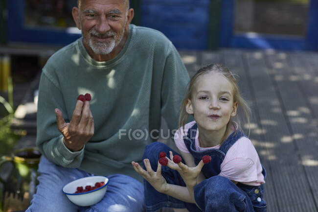 Дідусь з внучкою їдять малину на терасі в саду. — стокове фото