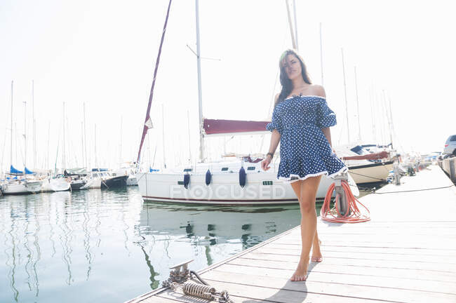 Jovem mulher vestindo vestido andando no molhe contra o céu claro durante o dia ensolarado — Fotografia de Stock
