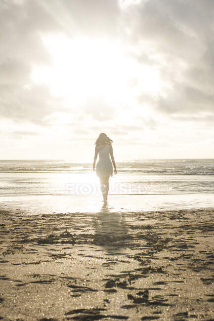 Young woman walking at beach against cloudy sky during sunset — Stock Photo