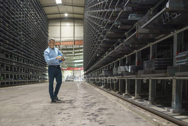Mature businessman using tablet in a high rack warehouse of a factory — Stock Photo