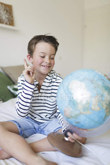 Portrait of smiling little boy sitting on bed with his globe — Stock Photo