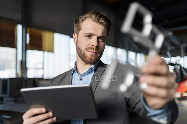 Jeune homme d'affaires avec tablette et pièce dans une usine — Photo de stock