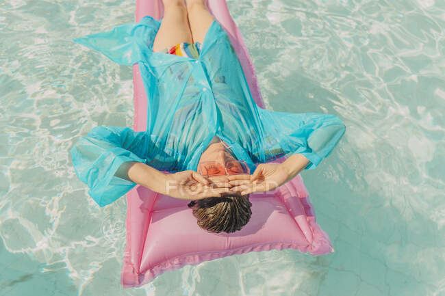 Donna con cappotto antipioggia blu rilassante sul lettino rosa in piscina — Foto stock