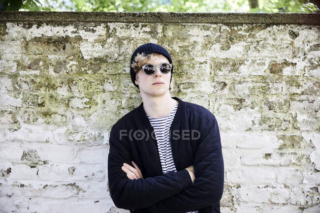 Ritratto di giovane uomo con cuffie con occhiali da sole e cappuccio davanti alla parete intemperie — Foto stock