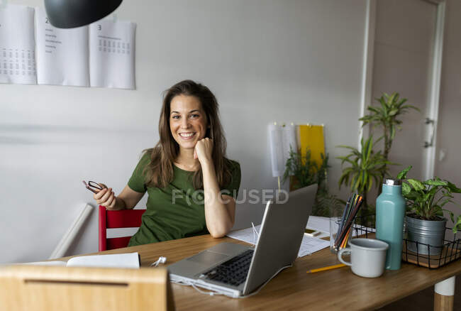 Donna d'affari sorridente seduta alla scrivania contro il muro in home office — Foto stock