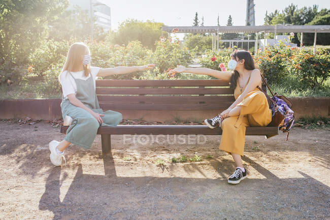Two friends wearing protective masks sitting on bench during Corona crisis and keeping distance — Stock Photo