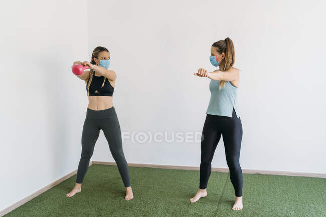 Woman wearing face mask exercising with coach at health club — Photo de stock