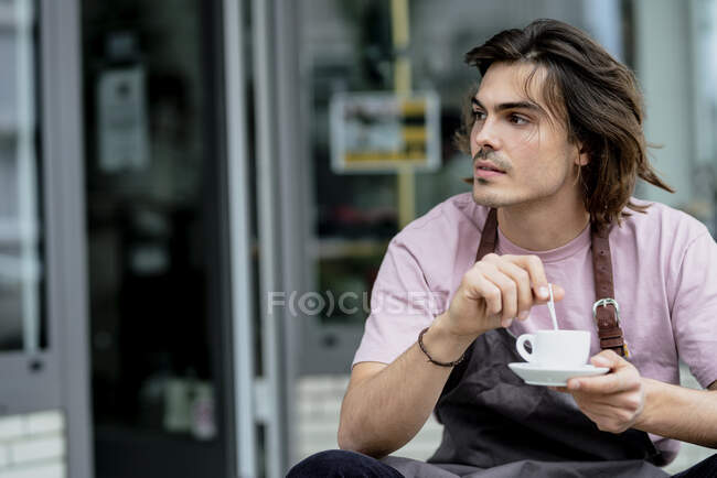 Pensiero proprietario maschio in possesso di tazza di caffè mentre seduto fuori caffè — Foto stock
