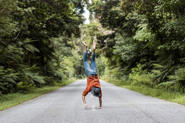 Young man performing handstand on country road amidst trees in forest — Stock Photo