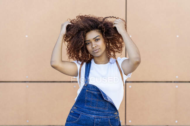 Впевнена молода жінка з руками в волоссі, що стоїть на стіні — стокове фото