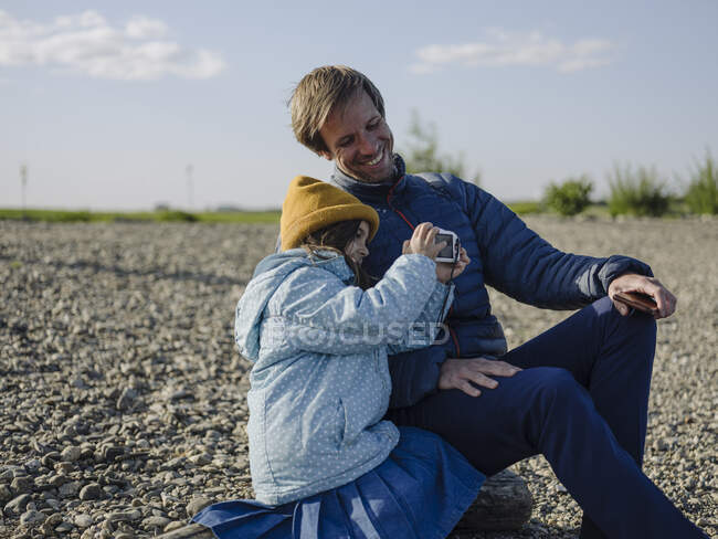 Feliz pai e filha fotografando com câmera enquanto sentados em terra contra o céu — Fotografia de Stock