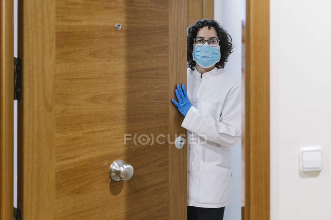 Médecin féminin portant un masque chirurgical debout à la porte de la clinique — Photo de stock