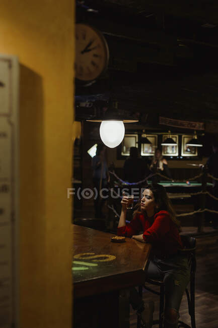 Грустная взрослая женщина держит пивной стакан, сидя за столом в ресторане — стоковое фото