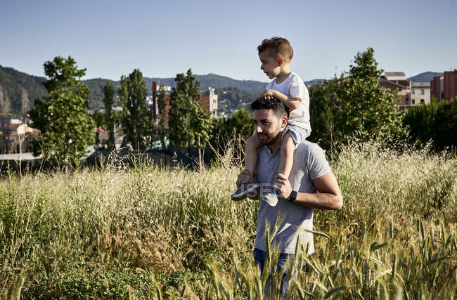 Padre che porta il figlio sulle spalle mentre cammina tra le piante contro il cielo limpido — Foto stock