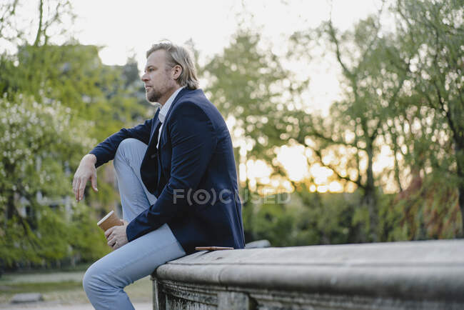 Hombre de negocios relajado con café para llevar en el parque de la ciudad - foto de stock