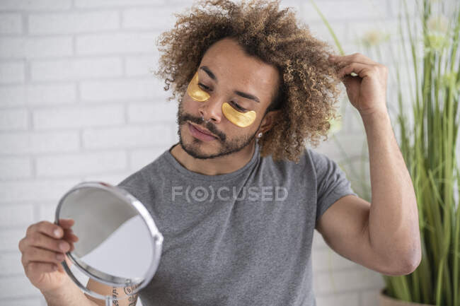 Gros plan d'un jeune homme avec des bandeaux sur le visage se regardant dans un miroir à la maison — Photo de stock