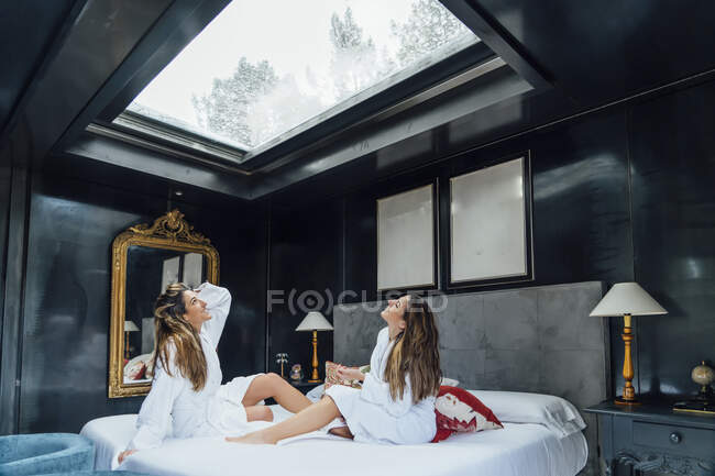 Twin sisters looking through skylight while relaxing on bed in hotel — Stock Photo