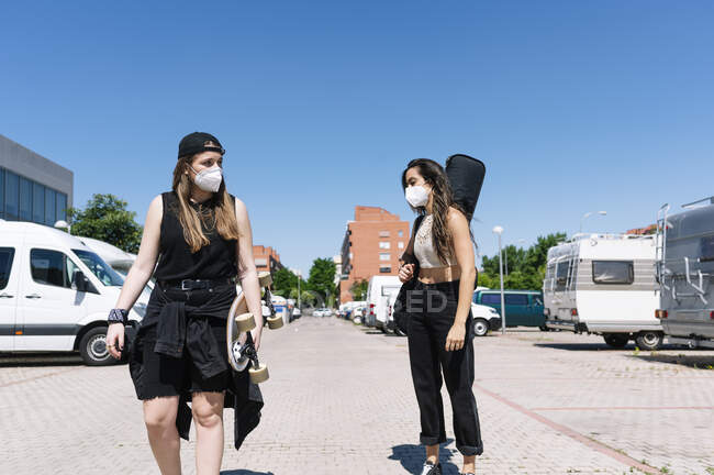 Dos mujeres con máscaras protectoras caminando por la calle - foto de stock