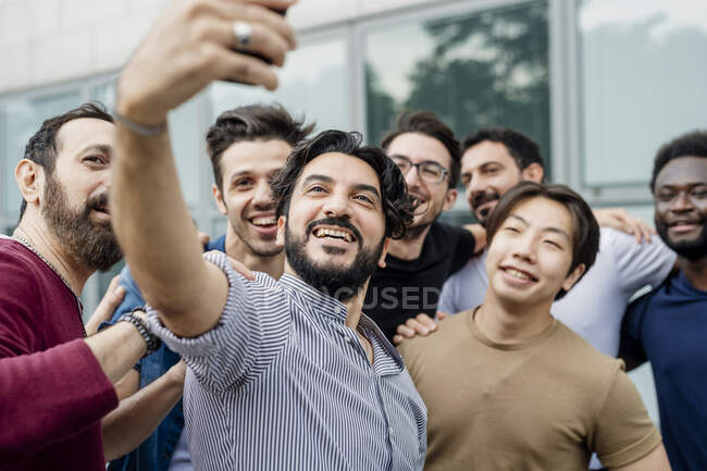 Веселий чоловік бере селфі з друзями-чоловіками, стоячи в місті — стокове фото