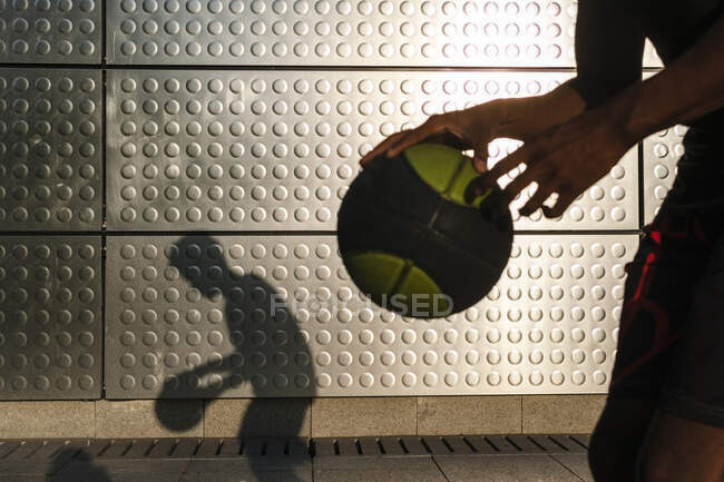 Молодой человек играет в баскетбол на металлической сияющей стене — стоковое фото