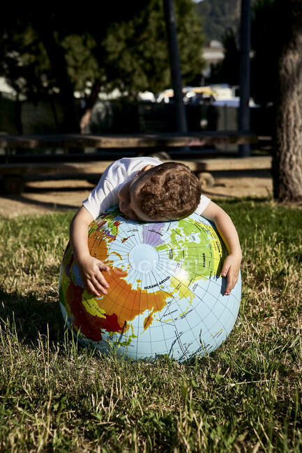 Boy embracing globe on grassy land in park during sunny day — Stock Photo