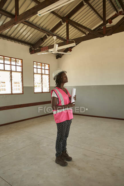 Arquitecta sosteniendo el plano de pie en el edificio de la escuela en la obra - foto de stock