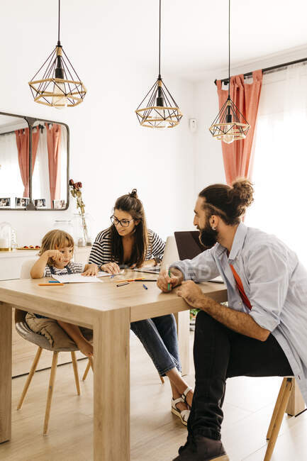 Parents looking at cute daughter painting on dining table at home — Stock Photo