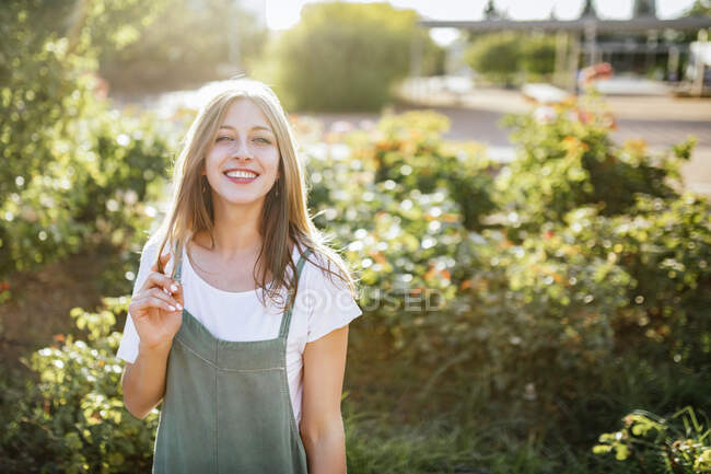 Portrait de jeune femme souriante dans le jardin public au contre-jour — Photo de stock