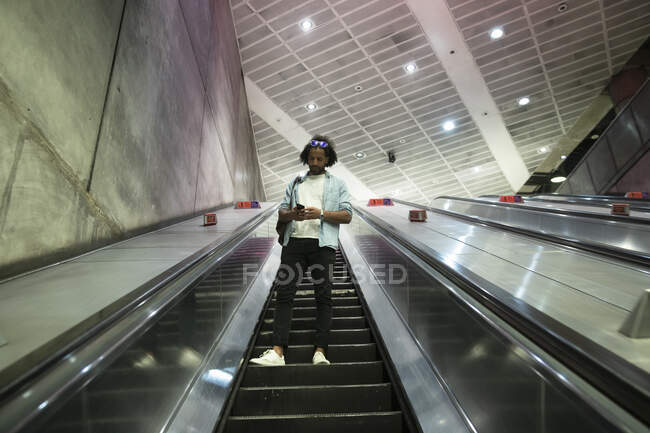 Young trendy man using smart phone on escalator at subway station - foto de stock