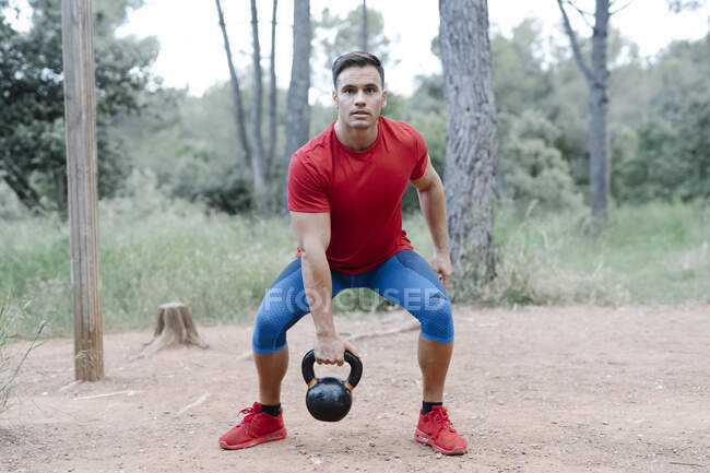 Young athletic man with dumbbell in the woods — Stock Photo