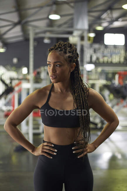 Confident female athlete with arms akimbo standing in gym — Stock Photo