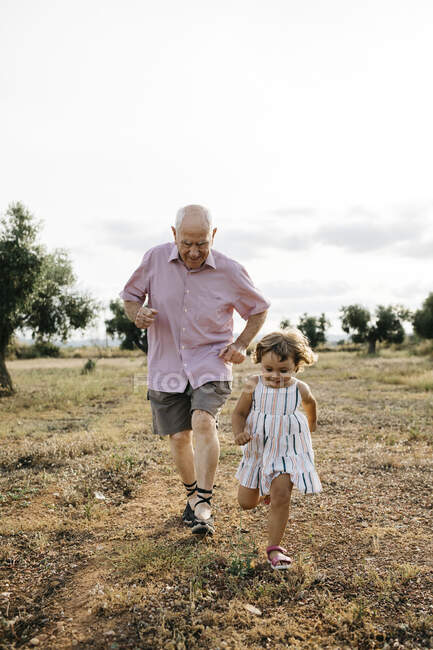 Nonno giocoso con nipote che corre sulla terra contro il cielo — Foto stock