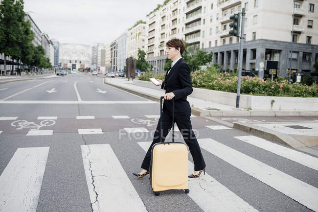 Businesswoman with suitcase crossing road in city — Stock Photo