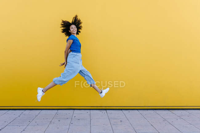 Bella donna che salta per la gioia davanti al muro giallo — Foto stock