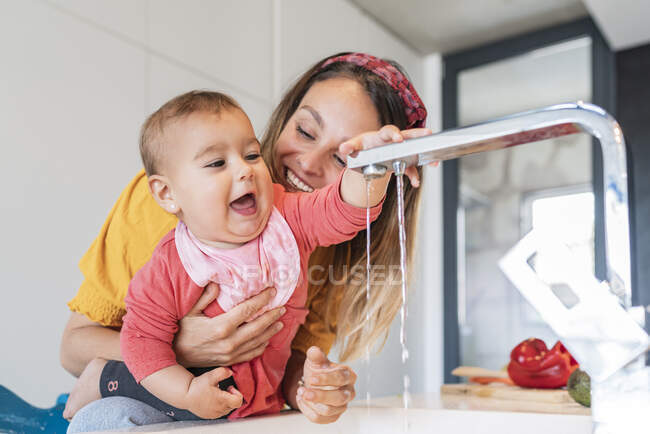 Nahaufnahme einer lächelnden Mutter, die in der Küche mit einem Wasserhahn spielt — Stockfoto