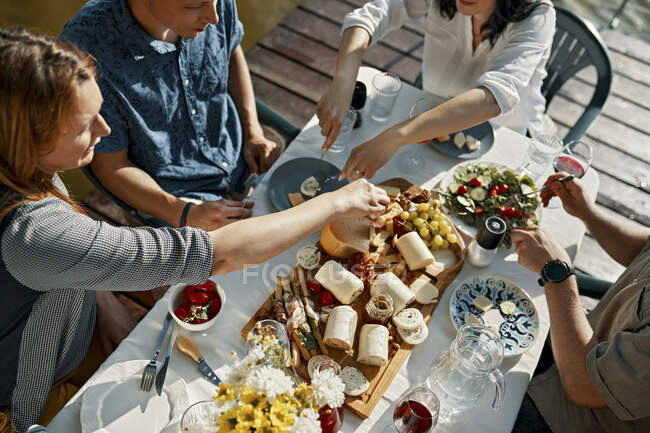 Amigos cenando con un plato de queso en embarcadero - foto de stock