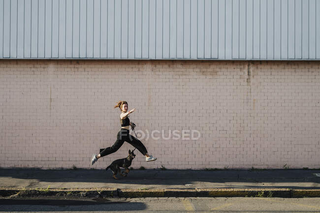 Mujer corriendo con perro en la acera contra la pared - foto de stock