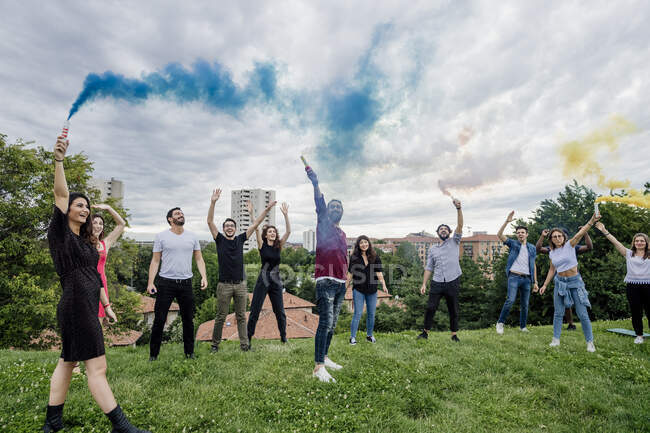Fröhliche Gruppe von Freunden spielt mit Rauchbomben im Park gegen bewölkten Himmel — Stockfoto