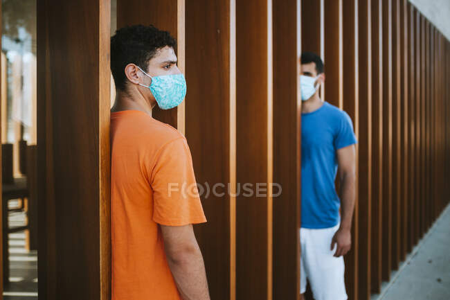 Male friends wearing masks standing by wooden built structure in city — Stock Photo