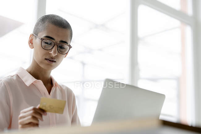 Businesswoman holding credit card and using laptop at desk in loft office — Stock Photo